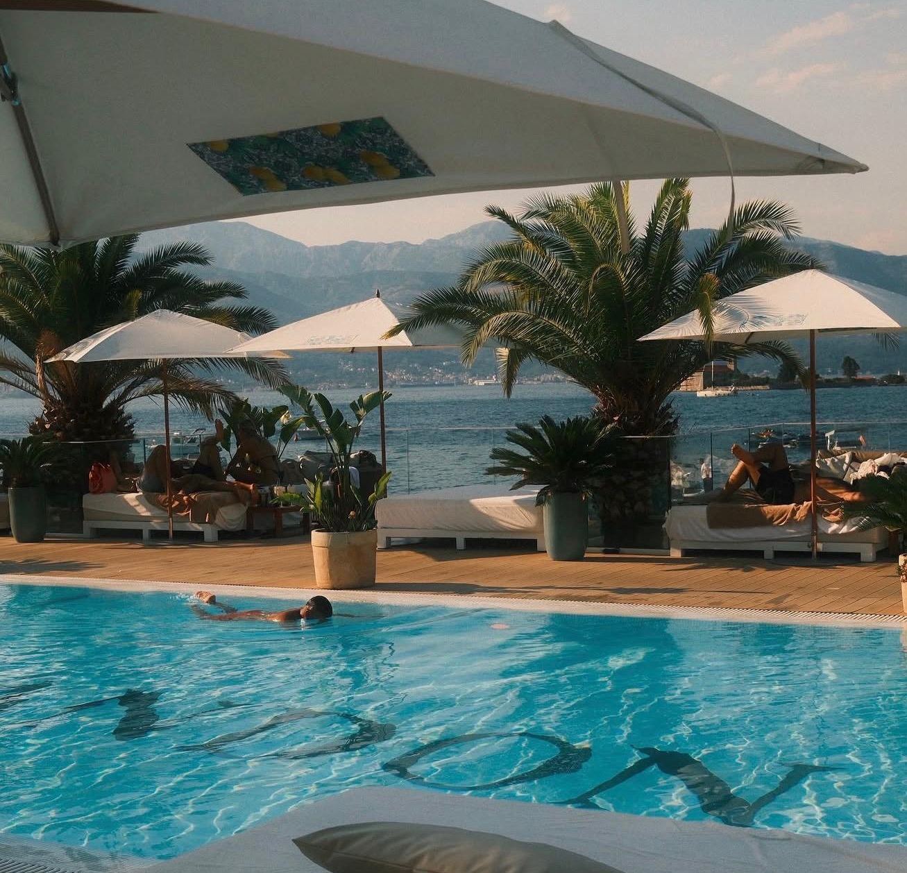 Bazen Monte Palm Beach pod suncobranom, kupač u vodi i more iza, Tivat