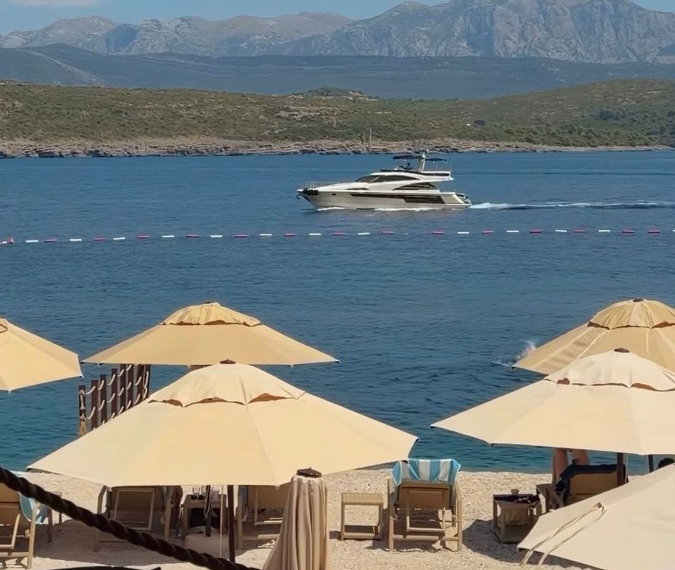 Plaža Signorina na Luštici, suncobrani i ležaljke uz vodu i jahta u prolazu