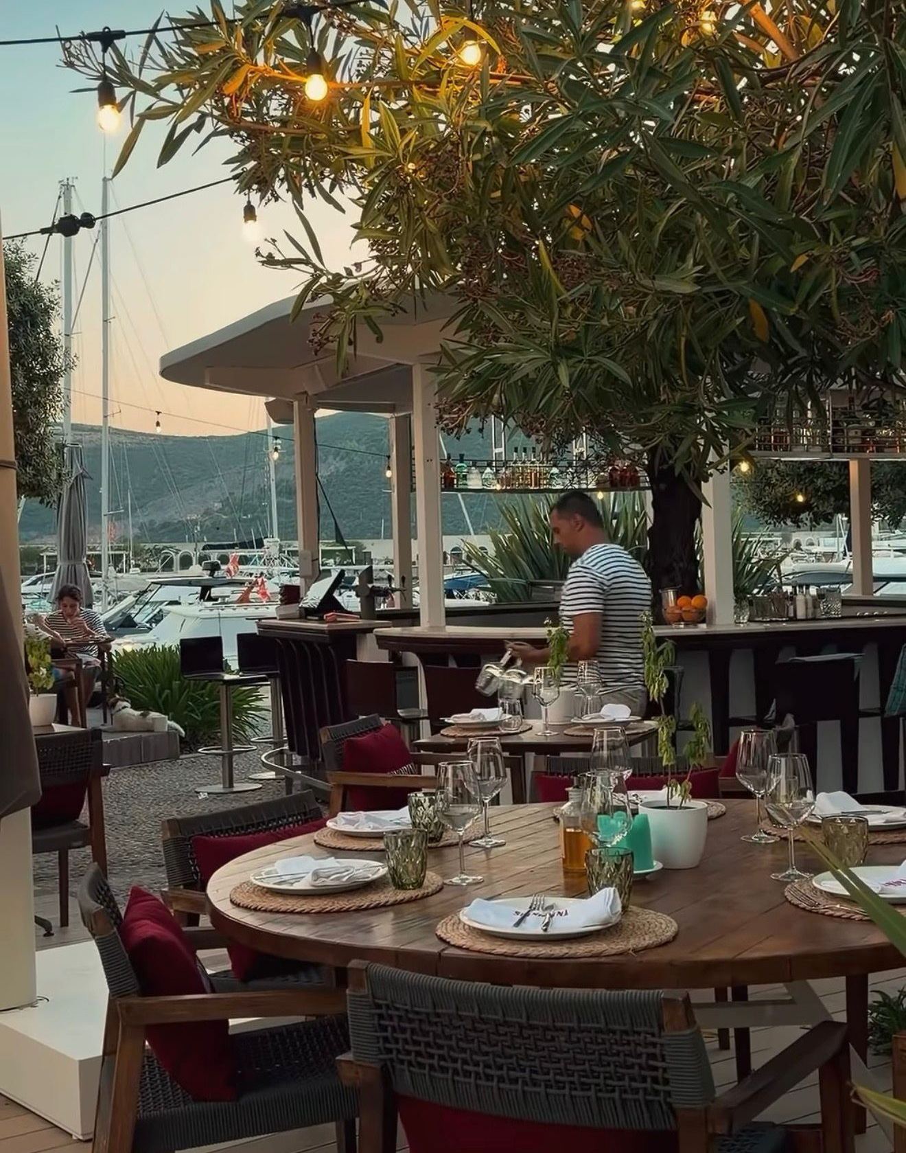 Postavljen sto na terasi restorana Signorina na Luštici, jarboli marine u sumrak