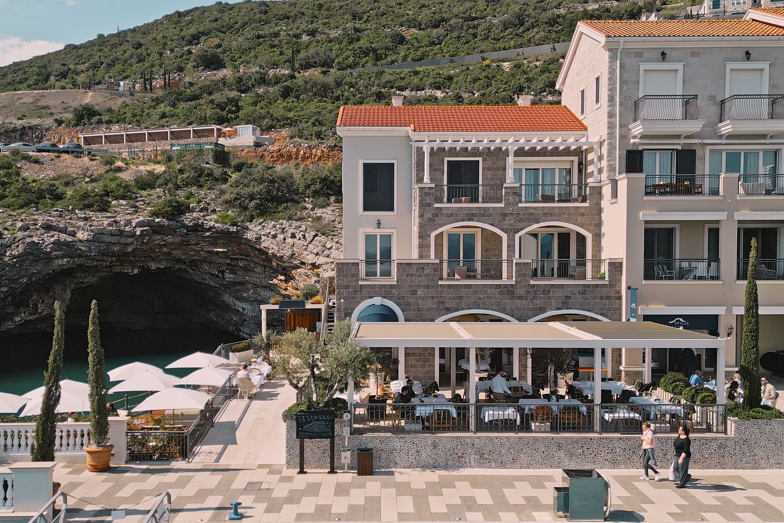Restoran Špilja u Luštica Bayu: kuća pod liticom, terasa i suncobrani uz vodu u Marina Villageu