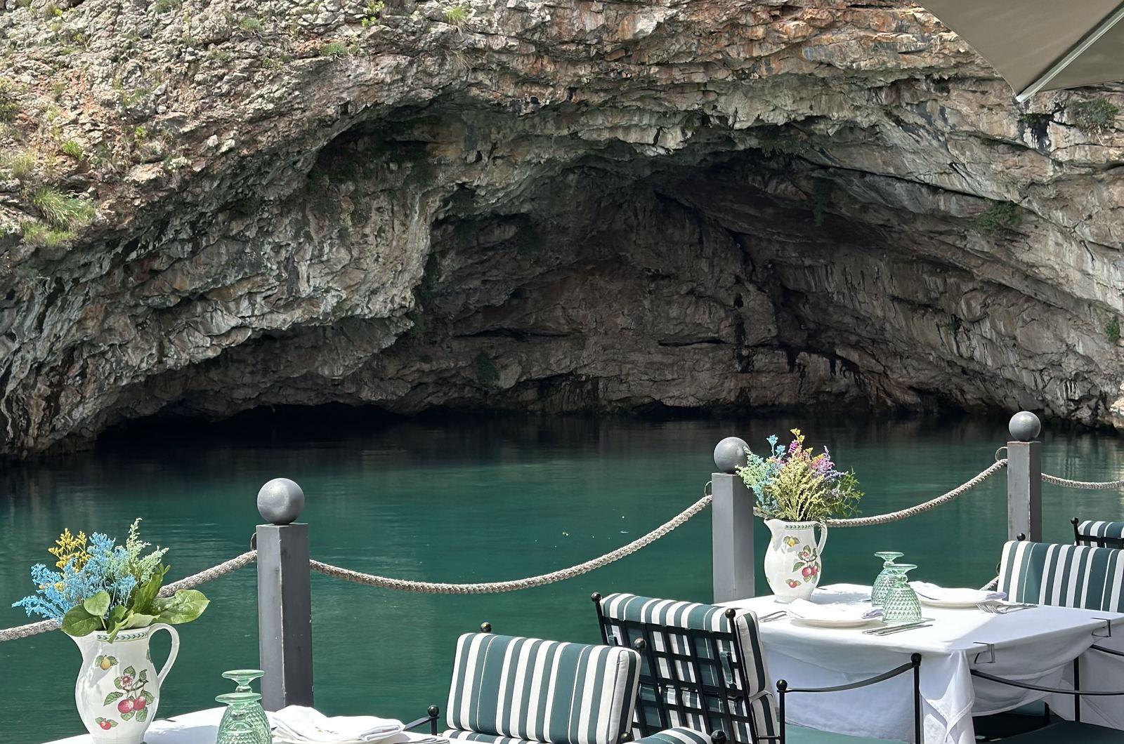 Postavljeni stolovi restorana Špilja ispred morske špilje u Luštica Bayu, zelena voda ispod