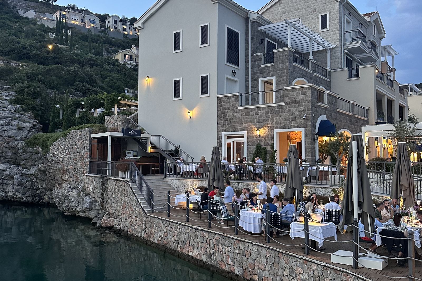 Osvijetljene terase restorana Špilja u Luštica Bayu u sumrak, iznad mirne vode